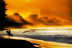 Winter Sunset: The last rays of sunlight slip between the front line of buildings on the Salinas beach, Asturias. Photo by Jaider Lozano #ocean #surfer #beach #rays #photography #sunset #waves #coast