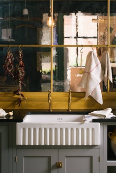 The Single Fluted Sink is from deVOL, as is all the hardware, including the Aged Brass Mayan Taps by Perrin & Rowe and the Hanging Rail. A partition featuring heritage glass separates the Real Shaker Kitchen from another kitchen just beyond it.