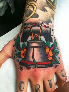 A tattooed man proudly displays his liberty bell tattoo on his hand, symbolizing freedom and individuality.