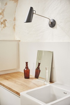 The Birdy Wall Light is seen again in the kitchen, along with a double-bowl farm sink and vintage glass vases.