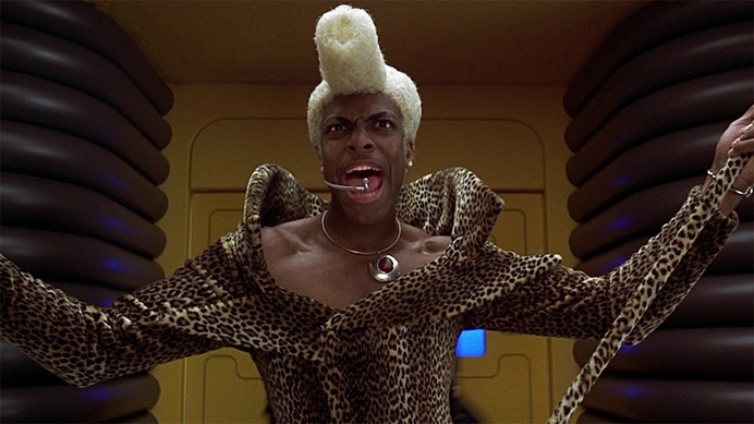 Ruby Rhod (Chris Tucker) speaking into a headset with arms stretched out