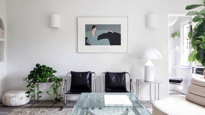 white living room with two leather chairs a glass coffee table and a few plants
