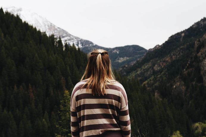 A woman standing back to camera and looking at snowy mountains behind the woods