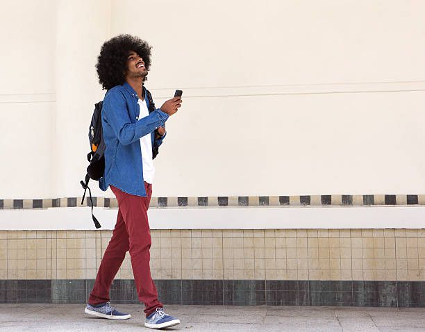 Smiling young black man walking with bag and mobile phone