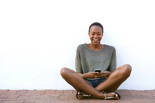 Happy young woman sitting on sidewalk with cell hone