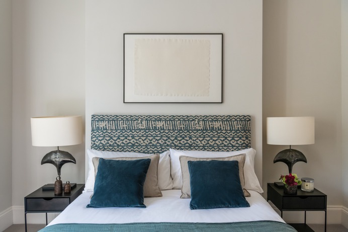 Olivia and her boyfriend's bedroom. Olivia stapled Khari blue linen fabric by Mark Alexander to an old headboard that once belonged to her mother. "I spent two months with different fabrics draped over the bed, testing out the styles," she shares. The Porta Romana lamps were scored at a sample sale; the bedside tables from La Redoute were purchased at a steep discount. The walls here are painted French Grey by Little Greene.
