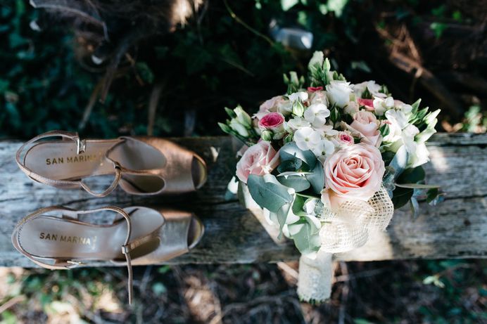 A pair of woman's shoes next to a magnificent flower bouquet on a wooden bench