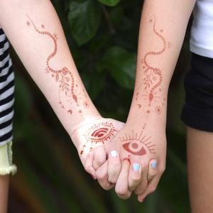 Sabrina - two girls holding hands with snake henna tattoos on arms A snake henna tattoo for your modern day witch. Our organic henna keeps you connected with nature as you create your own henna art with Mihenna stencils.