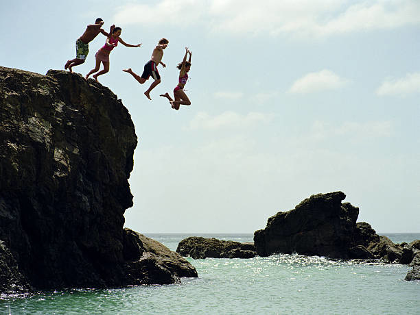 Group of friends jumping into ocean from rock cliff