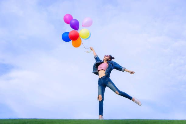Young Woman Holding Colorful Balloons While Standing Against Sky