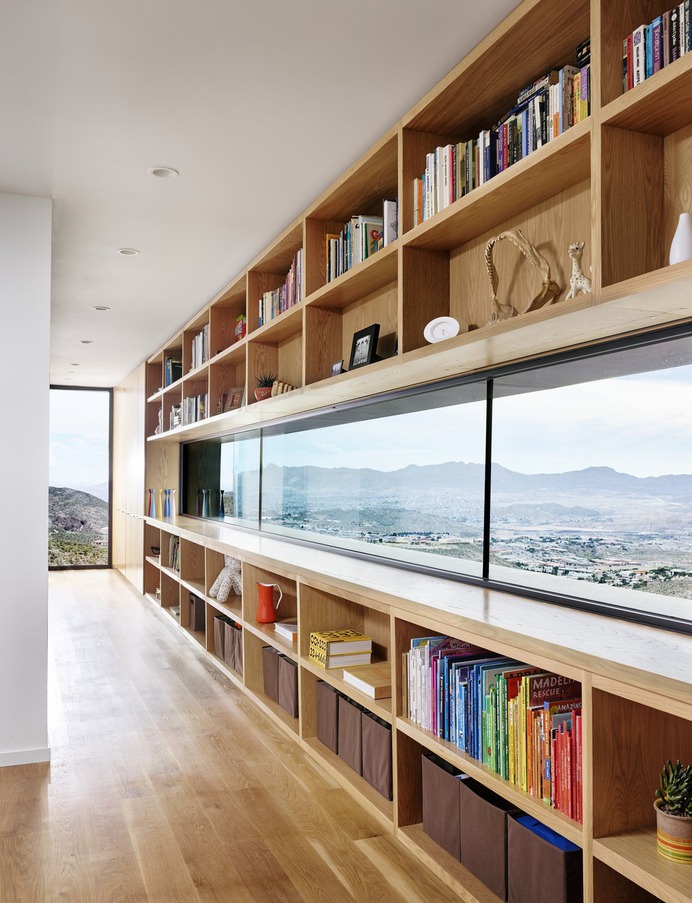 The home's elevated upper volume dramatically perches above a canyon 30 feet below. Horizontally stretched Series 670 Fixed Windows offer postcard views of downtown El Paso and Juarez. At the end of the hallway, another fixed window precariously overlooks a steep drop to the canyon below. "There are constantly little nose smudges on the window because the best way to experience this lookout point is to press yourself right up to the glass and feel like you're flying," say Dale and Darci. Photo 10 of 11 in A Cleverly Camouflaged Family Home Floats Above the West Texas Mountainside