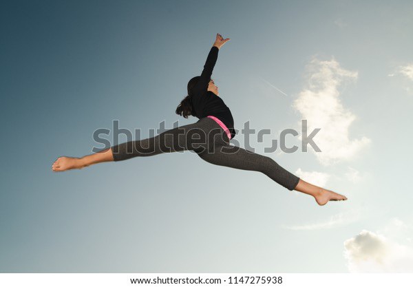 Smiling, happy young girl gymnast acrobat jumping high in the sky.