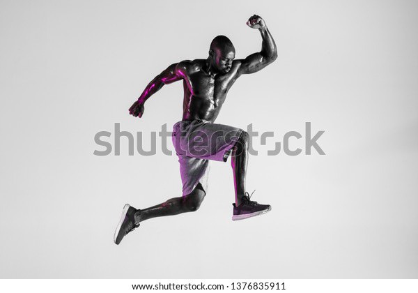 Win of the feelings. Young african-american bodybuilder training over grey studio background. Muscular single male model jumping in sportwear. Concept of sport, bodybuilding, healthy lifestyle.