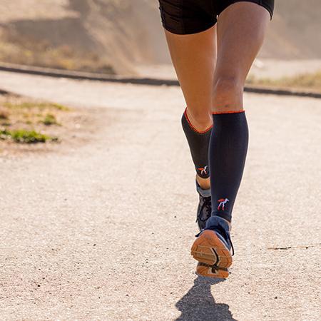 Close-up of runner's legs wearing compression calf sleeves in solid slate with Lily Trotters' bird logo at ankle