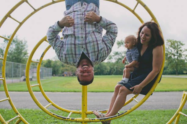 Mother and son looking at father hanging on circular monkey bars in playground