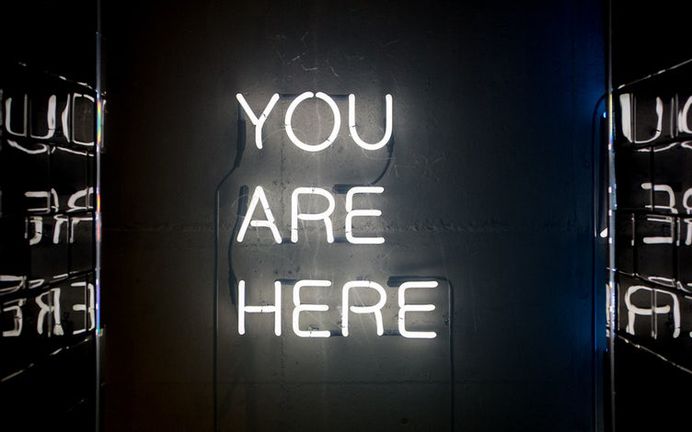 A white neon reading "you are here" on a wall