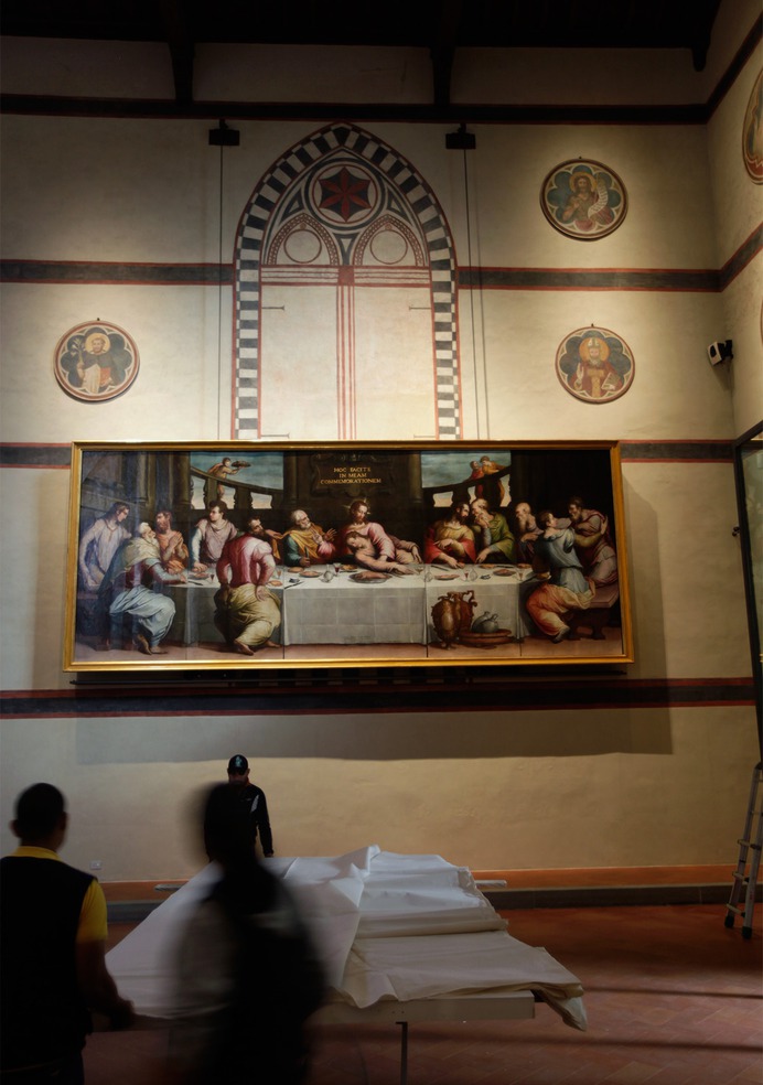 A painting of the las supper hangs high on the wall of a low-lit, churchlike interior