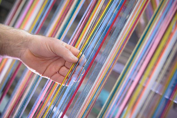 Worker adjusting multicoloured silk yarn on industrial loom in textile mill