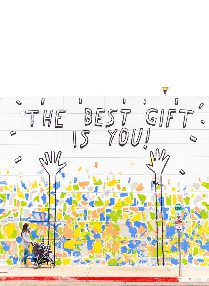 Woman pushing a stroller passes mural that reads "The best gift is you"