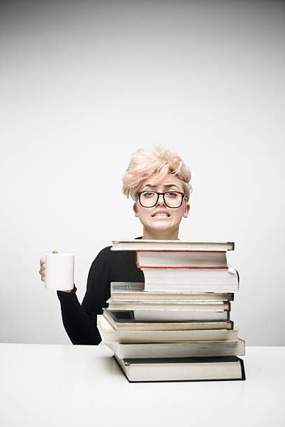 Young Woman Drinking Coffee Behind Pile of Textbooks