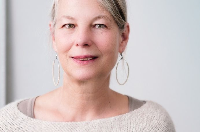 A white old woman wearing a sweatshirt and circular earrings smiling.