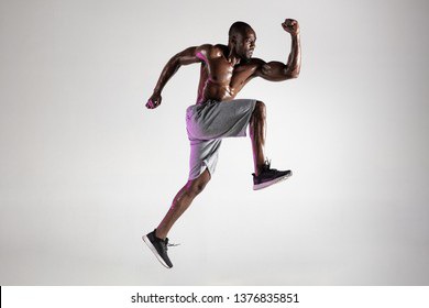 Run for adventures. Young african-american bodybuilder training over grey studio background. Muscular single male model jumping in sportwear. Concept of sport, bodybuilding, healthy lifestyle.