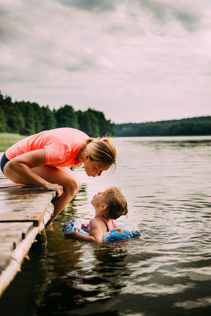 Mother encourages her child swimming in a lake