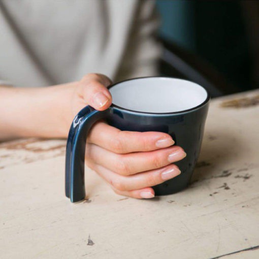 The E-Mug features a long open handle that touches the table for added support when you put it down. Its ergonomic shape is designed for children and the elderly with a weak grip. It's also stackable and microwave-safe. Made from Hasami porcelain in Japan.