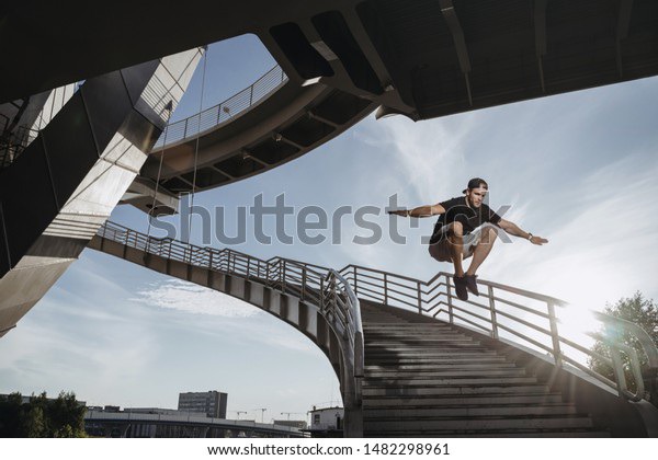 Parkour athlete training in the city. Man performs a big freerunning jump through the stairs.