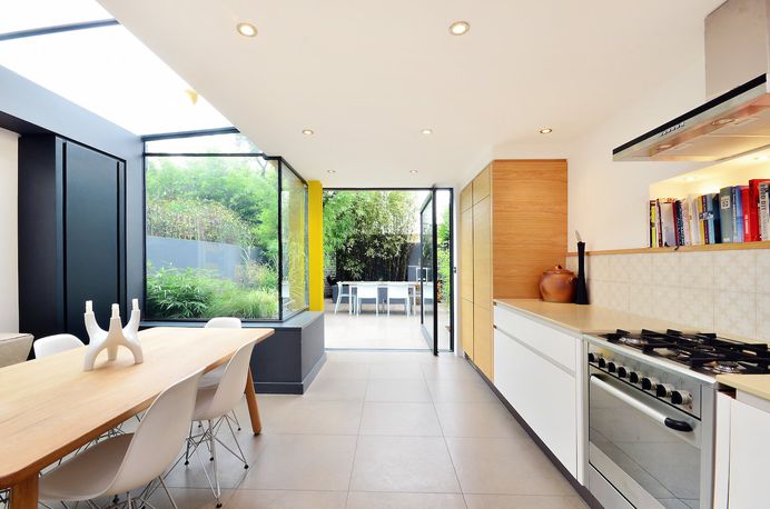 The fridge is tucked behind the bespoke oak cupboard. Tagged: Kitchen, Engineered Quartz Counter, Refrigerator, Ceramic Tile Backsplashe, Recessed Lighting, Ceramic Tile Floor, Range, Range Hood, Wood Cabinet, White Cabinet, Wall Oven, and Accent Lighting. Photo 3 of 10 in A London Home With a Nightclub–Inspired Kitchen Is Listed For $2M