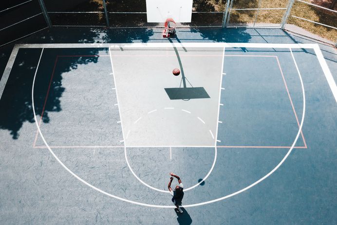 Drone view of person shooting basketball into hoop on a court outdoors