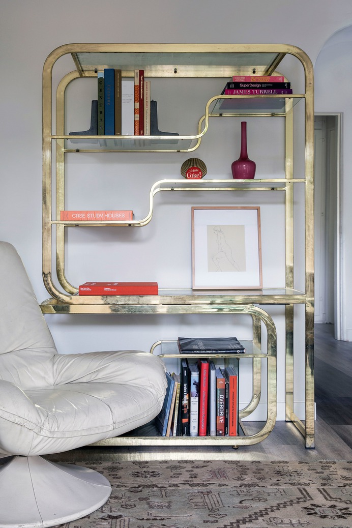 gold bookshelf with books vase and art next to white chair