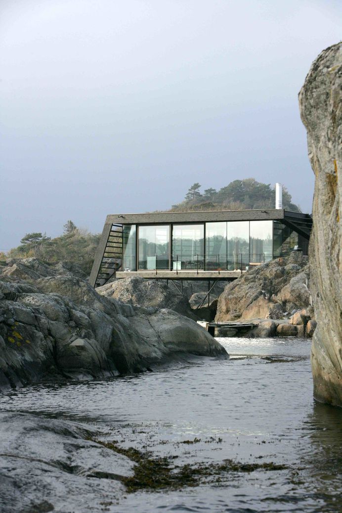 Balancing on irregular, rough-hewn rocks along the Norwegian coast, this renovated summer cabin near a town called Larvik in Vestfold County intelligently navigates a challenging terrain to take full advantage of dramatic views. Located just about 16 feet from the sea, Lille Arøya—a 807-square-foot summer cabin—perches on a small, rugged island. Oslo-based practice Lund Hagem Architects took on the challenge, drilling solid galvanized steel columns straight into the rock to provide stable support for the house on the uneven ground. They built a new structure that consists of two volumes:a lower post-and-beam volume where the bedrooms and bathrooms are located, and a taller volume with a large, cantilevered roof with wind-bracing gables that serves as shelter for the living, kitchen, and dining areas. Glulam beams are used inside and out, and both interior and exterior walls are clad in rough sawn ore pine. Together with the raw steel columns and white concrete fireplace, the wood defines the color and mood of the interiors. The uniform aesthetic of the cabin's interior and exterior dissolves the threshold between indoor and outdoor spaces—and further connects the structure with its stunning, coastal landscape. Tagged: Exterior, House, Cabin Building Type, Flat RoofLine, and Green Roof Material. Photo 7 of 11 in Dwell's Top 10 Cabins of 2017 from A Norwegian Summer Cabin Embraces the Rocky Terrain