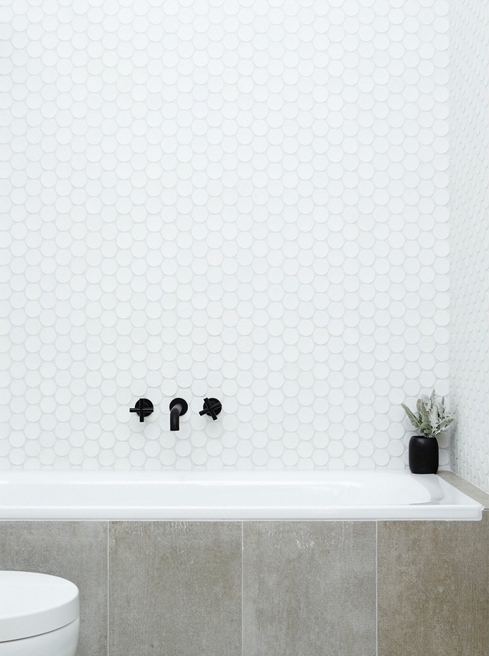 Bathroom with concrete bathtub siding, circular mosaic tile wall with white grout, and black details. Paddington Terrace by TomMarkHenry.