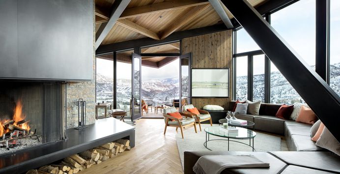 An Angular Mountain Retreat in Colorado Captures Breathtaking Views. Living Room, Sectional, Coffee Tables, Chair, Standard Layout Fireplace, Rug Floor, Recessed Lighting, Ottomans, Wood Burning Fireplace, and Medium Hardwood Floor.