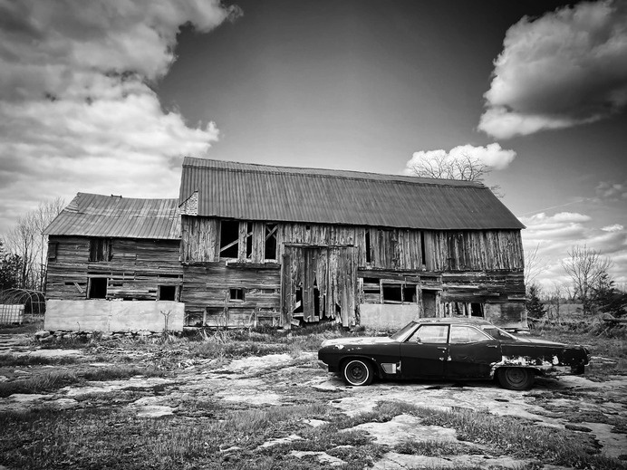 Stunning BW photo of a beaten down car in front of a barn. Photo by Roberto Scozzari