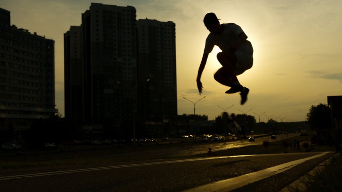 Man in White Long Sleeve Shirt and Black Pants Jumping on Gray Asphalt Road