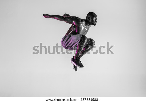 Flight of freedom. Young african-american bodybuilder training over grey studio background. Muscular single male model jumping in sportwear. Concept of sport, bodybuilding, healthy lifestyle.