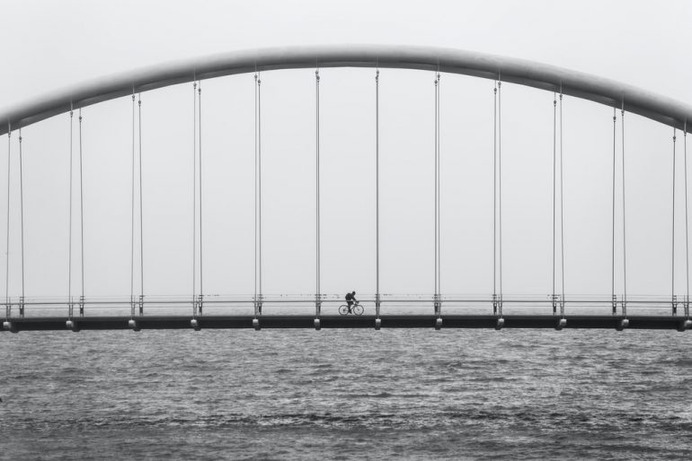 gray scale photo of person driving bike on bridge