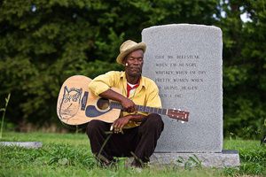 Photo of Mississippi blues musician, guitar player Pat Thomas at his Dad's grave , photographed in Leland, MS in the delta along the Blues Highway, Highway 61 near The Crossroads. Photographed for Moonshine & Mojo Hands. Pat Thomas is the Son of James "Son" Thomas, the legendary bluesman. Environmental portrait. We are an industrial photographer, on location photographer & location commercial photographer. Shallow depth of field and selective focus.
