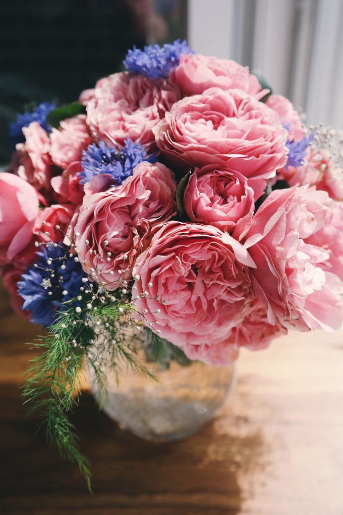 A vase with large pink peony flowers and smaller white and violet flowers