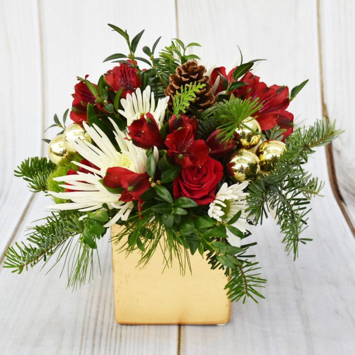 ADD A TOUCH OF THE HOLIDAY SPARKLE WITH THIS ARRANGEMENT FEATURING ASSORTED PINES, SHORT STEM ROSES AND MINI GREEN HYDRANGEA. CONTAINER COLOR MAY VARY.