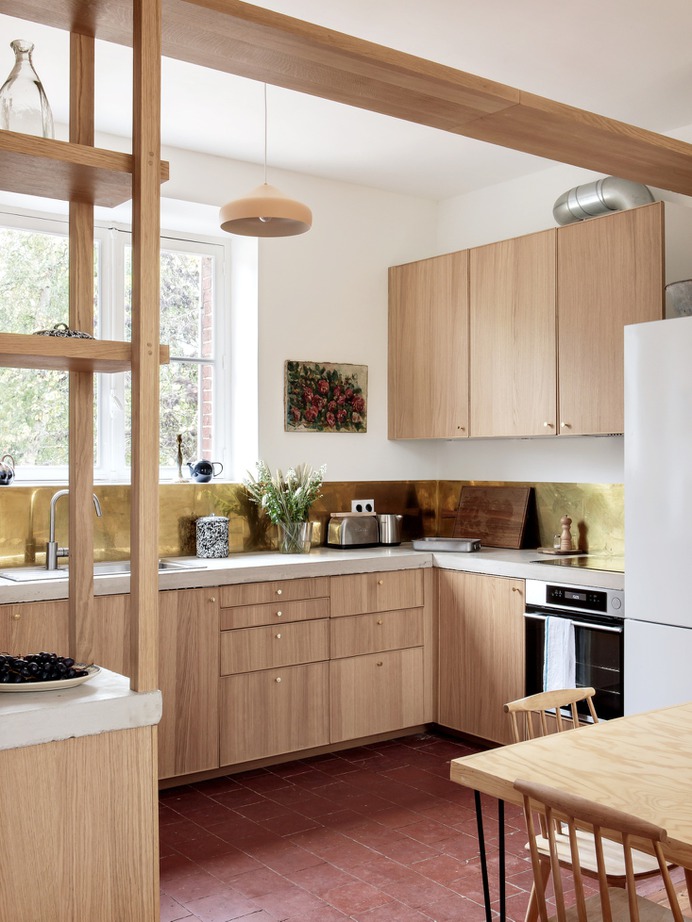 Oak display shelves divide the dining area from the kitchen. The oak-fronted Ikea cabinets are topped with a concrete counter fabricated in Paris. Feilders sourced the brass backsplash from Tartaix, a Paris metal store in business since 1919.