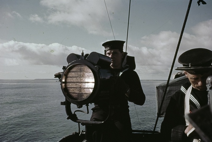 A signaller operates an Aldis lamp on board a British warship, 1942.