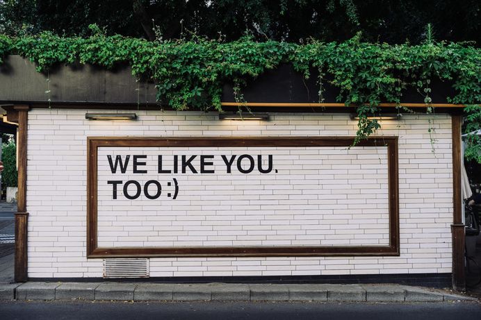 “We like you too :)” written on a white brick wall