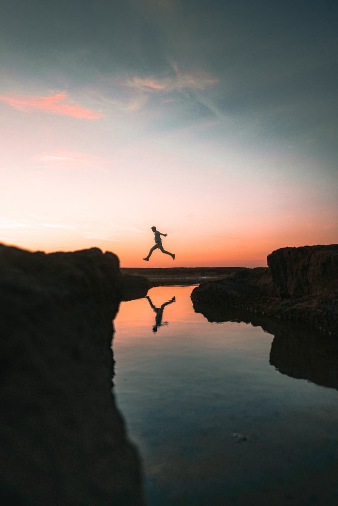 Man Standing on Rock Formation Near Body of Water during Sunset